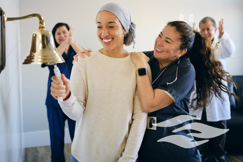 An adult woman chemotherapy patient in a treatment office, celebrating the completion of her treatment with a ceremonial bell ring.