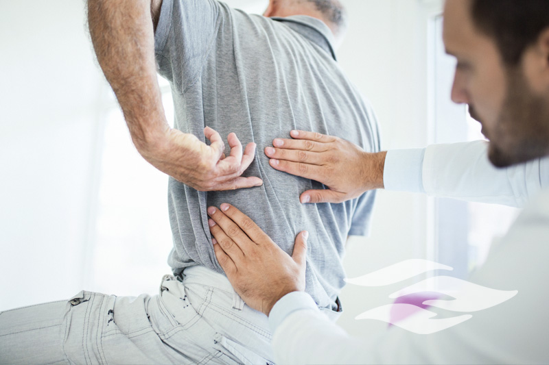 Closeup rear low angle view of an early 60's senior gentleman having some back pain. He's at doctor's office having medical examination by a male doctor. The patient is pointing to his lumbar region.