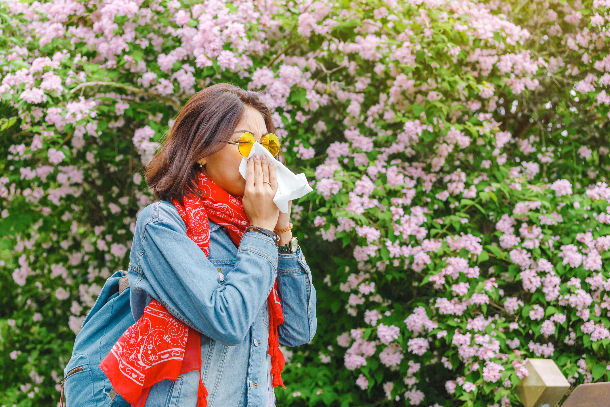 Woman sneezes into tissue while surrounding by blooming plants and flowers