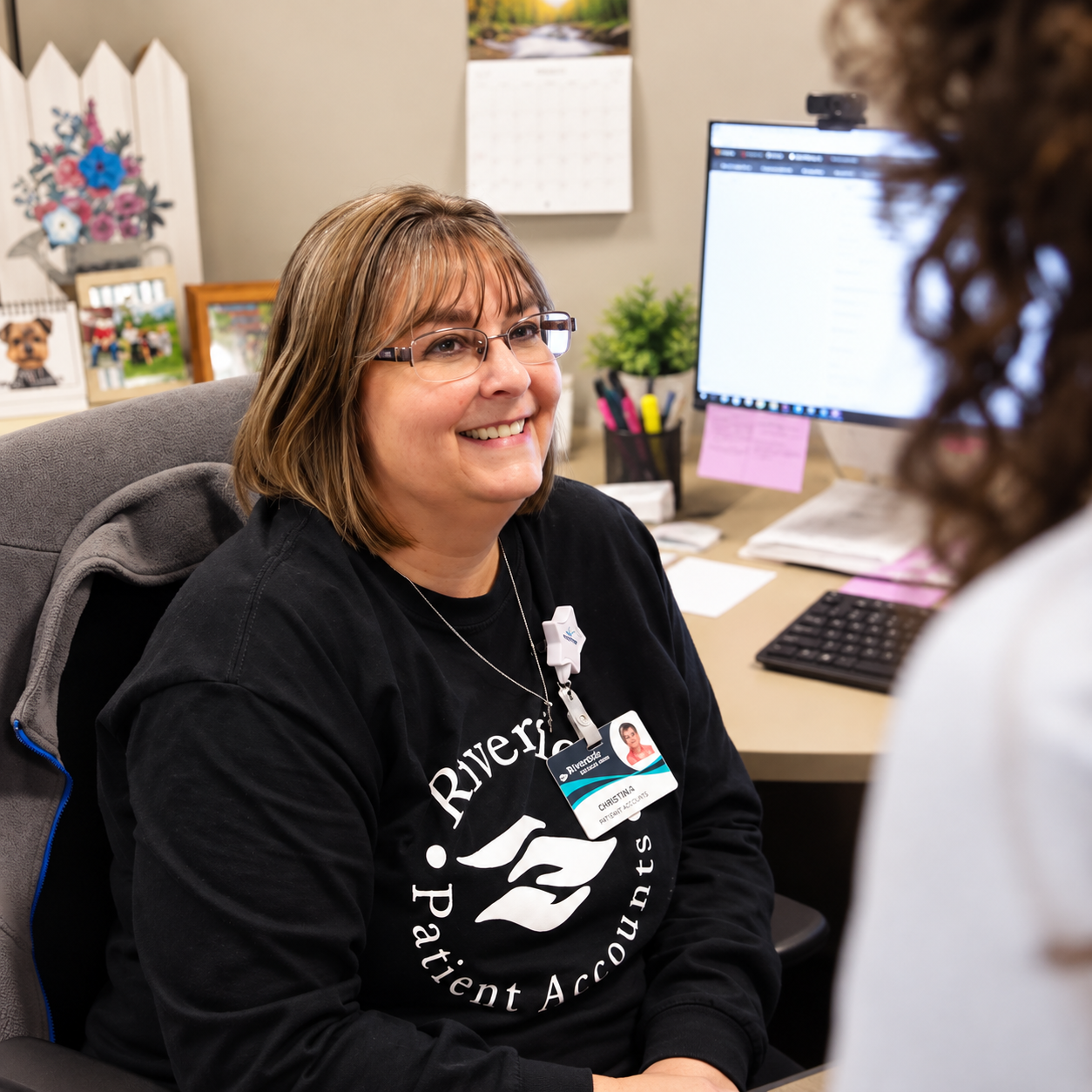 Smiling Riverside Patient Accounts team member talking with a coworker at her desk