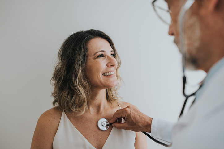 woman smiles while having heart and lungs checked by doctor